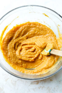 A glass bowl filled with a pumpkin mixture and a spatula.