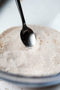 A pumpkin spice mixture in a glass bowl. There's a spoon in the bowl as well.