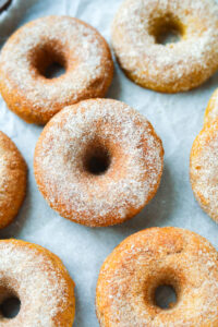 A pumpkin spice donut laid on top of another pumpkin doughnut. There are other donuts around them as well.