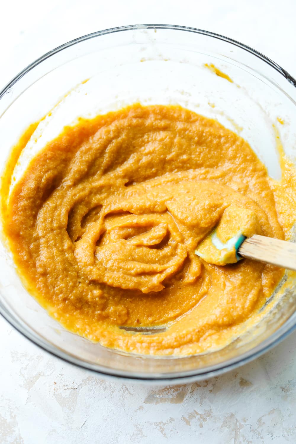 A glass bowl filled with a pumpkin mixture and a spatula.