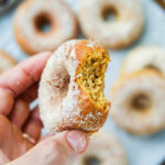 A hand holding a donut with a bite taken out of it.