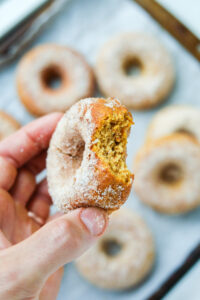 A hand holding a donut with a bite taken out of it.