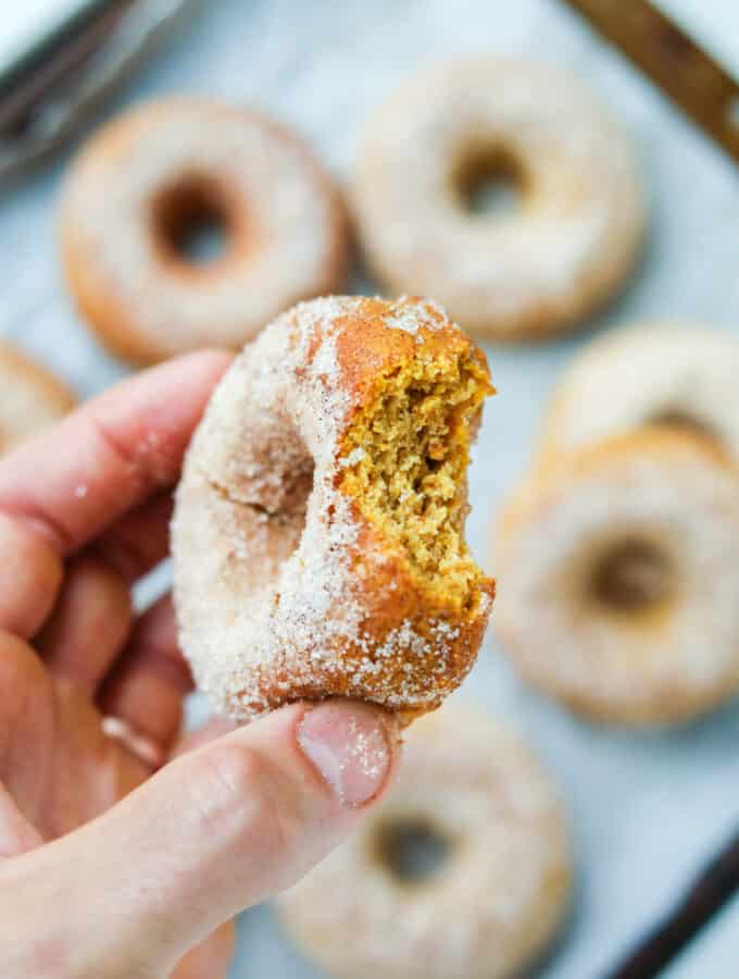 A hand holding a donut with a bite taken out of it.