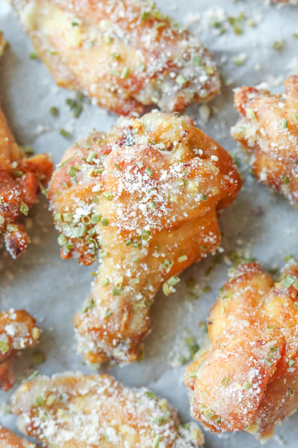 A garlic parmesan drum chicken wing on a piece of white parchment paper.