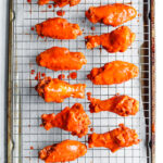 11 Chicken wings covered in hot sauce on a wire rack set over a baking sheet.