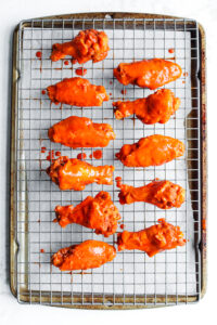 11 Chicken wings covered in hot sauce on a wire rack set over a baking sheet.