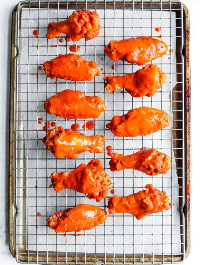 11 Chicken wings covered in hot sauce on a wire rack set over a baking sheet.