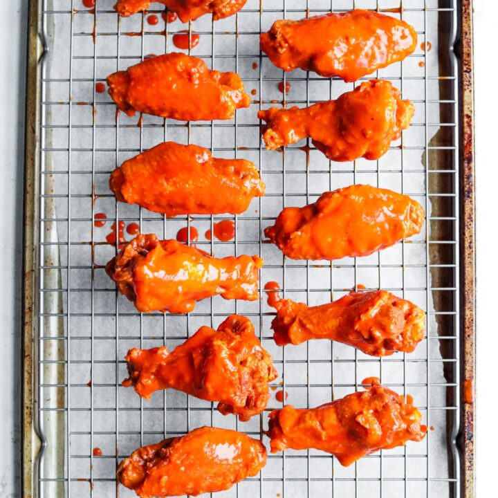 11 Chicken wings covered in hot sauce on a wire rack set over a baking sheet.