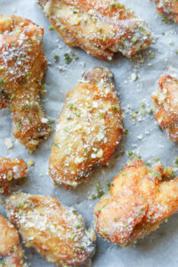 A garlic parmesan chicken wing on a white piece of parchment paper.