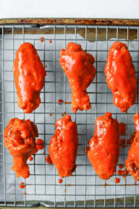 Chicken wings coated in hot sauce on a wire rack.