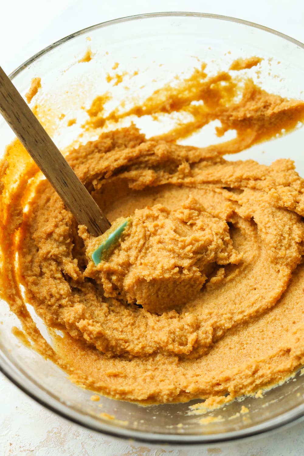 Pumpkin batter in a glass bowl. There's a turquoise spatula in the bowl as well.