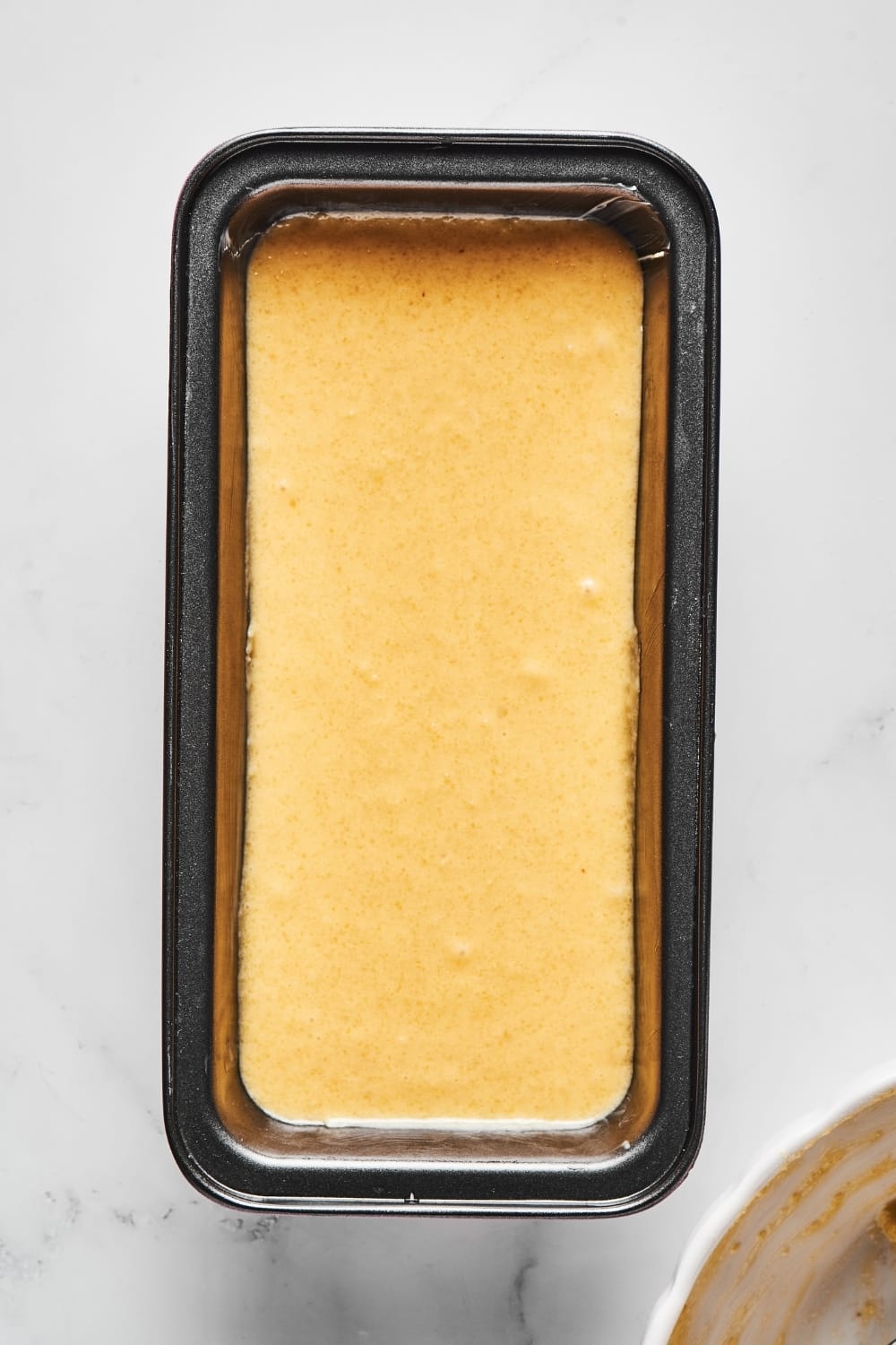 A loaf pan on a white counter filled with pound cake batter.