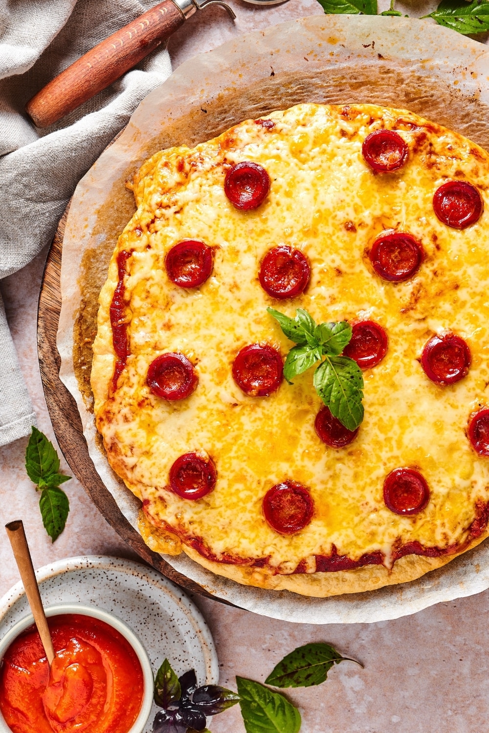 A chicken crust pizza with cheese and pepperoni on a piece of parchment paper on a pizza sheet.