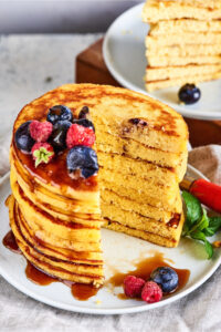 Eight cream cheese pancakes stacked on top of one another on a white plate. There is a triangle cut out of the pancakes and the inside of the pancake stack is showing.