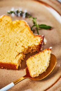 Part of a slice of poundcake lying flat on a brown plate. There is a spoon with a piece of the poundcake on it.