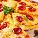 Chicken crust pizza cut into slices on a piece of parchment paper.