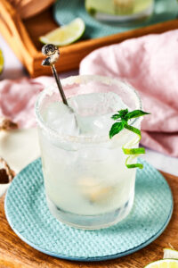 A wooden board with a circular blue coaster on it with a glass of margarita on top.