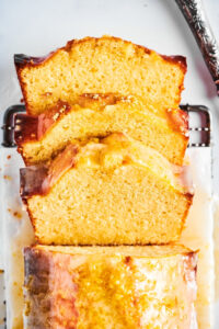 Part of the top of a pound cake loaf with three slices cut out leaning against one another in front of the loaf. The loaf is on a piece of parchment paper on top of a black wire rack on the white counter.