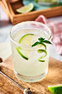 A glass of margarita with a lime wedge in it on a wooden board.