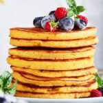 A stack of eight cream cheese pancakes on a white plate.