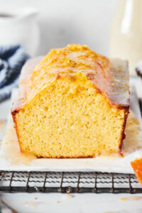 Pound cake loaf with a slice out of the front of it on a piece of parchment paper on a black wire rack.