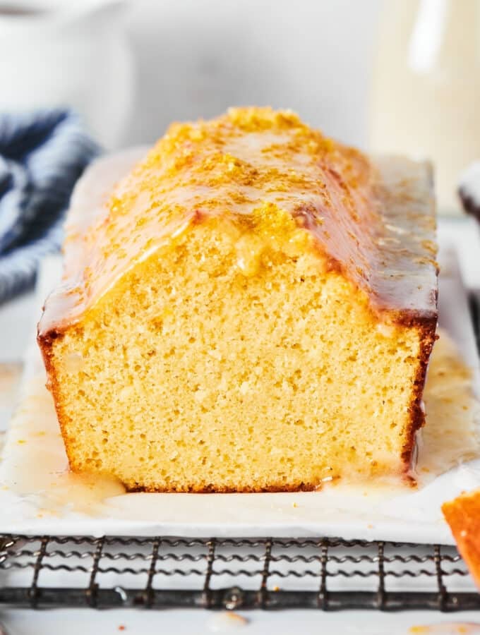 Pound cake loaf with a slice out of the front of it on a piece of parchment paper on a black wire rack.