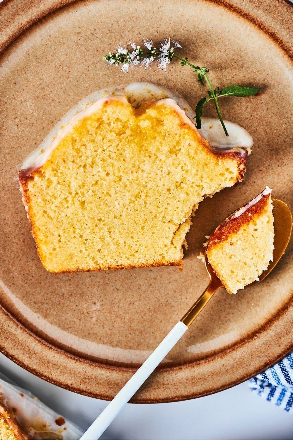 Thick slice of pound cake lying flat on a brown plate. There is a spoon on the plate with a piece of the bottom right corner of the poundcake on it.