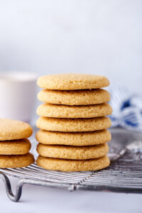 Seven shortbread cookies stacked on top of one another on a wire rack on a white counter. Next to it is part of three shortbread cookies stacked on top of one another.