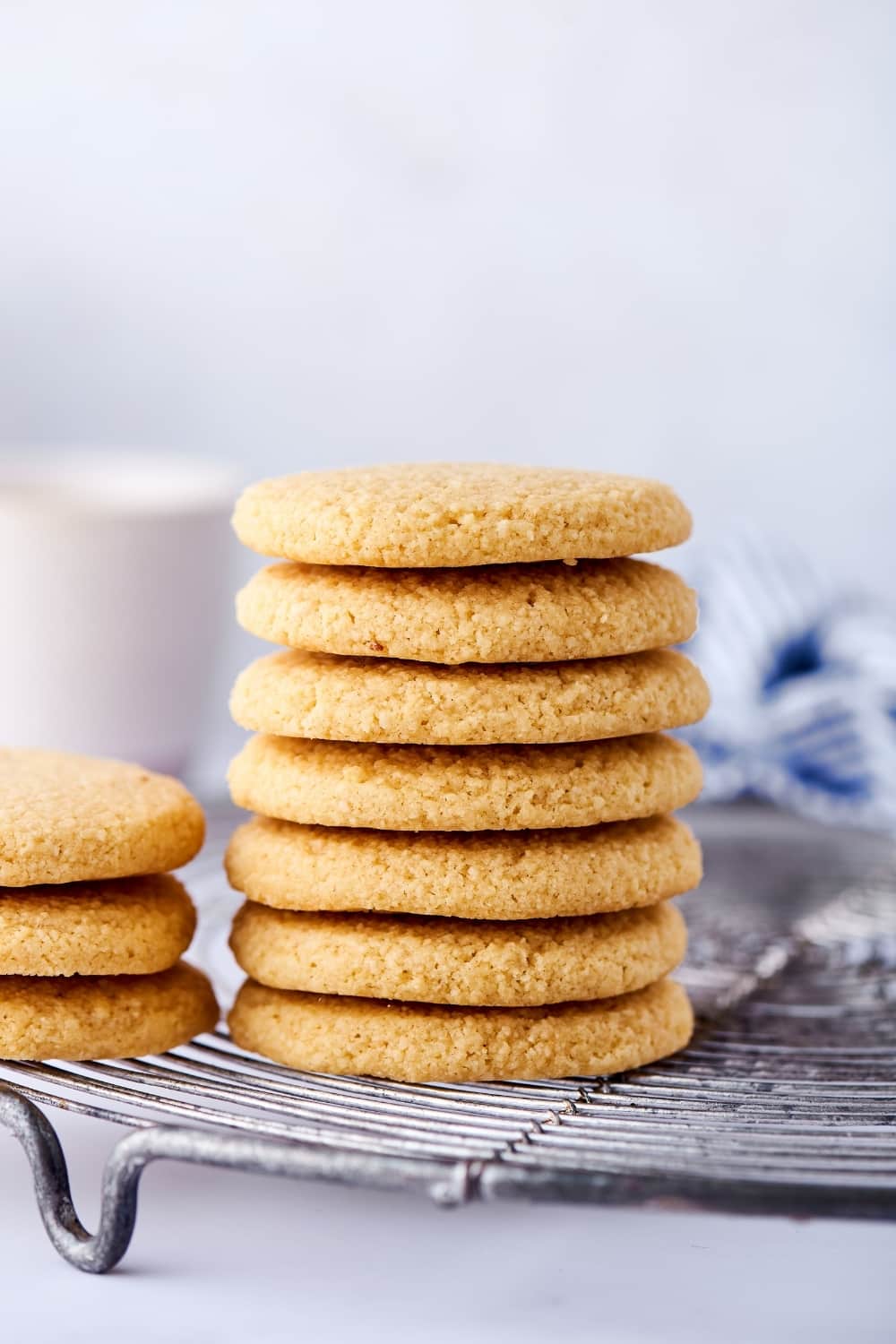 Seven shortbread cookies stacked on top of one another on a wire rack on a white counter. Next to it is part of three shortbread cookies stacked on top of one another.