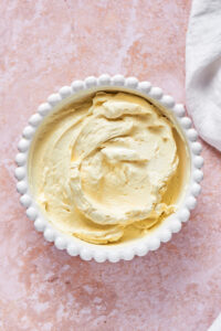 A white bowl and a pink counter filled with cream cheese frosting.