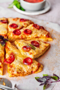 Four slices of cheese and pepperoni chicken crust pizza on a piece of parchment paper.