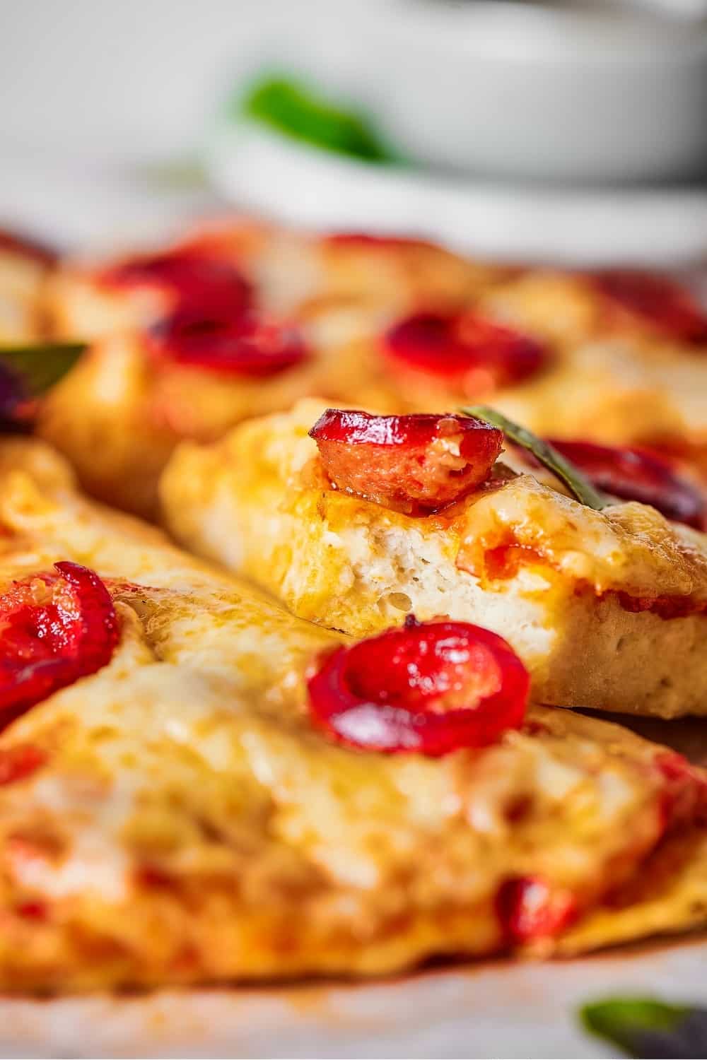 A slice of cheese and pepperoni chicken crust pizza with a bite out of the front on top of another slice of pizza.