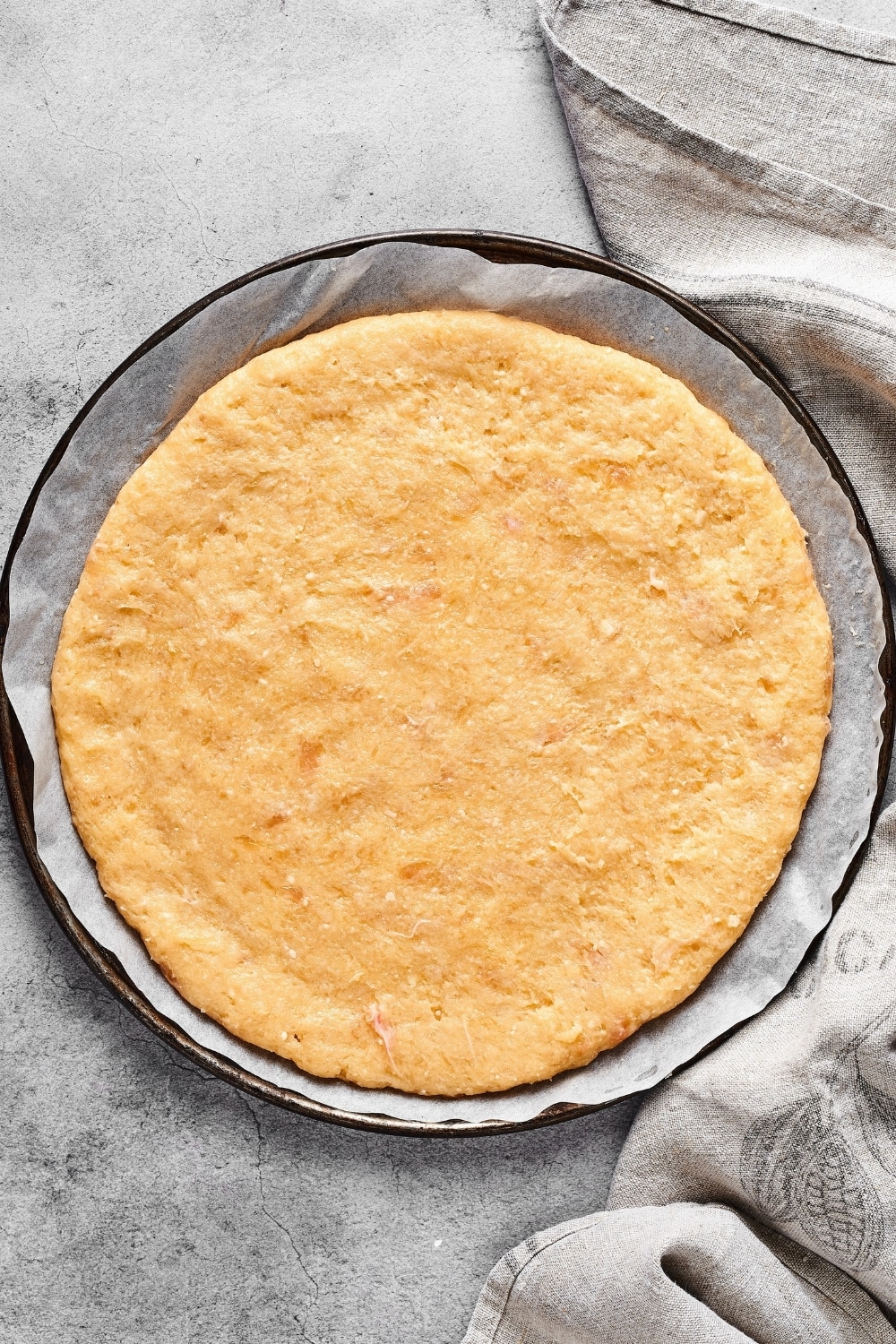 A chicken crust pizza on a piece of parchment paper on a pizza tray on a grey counter.