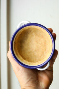 A hand holding a small bowl that has a pie crust in it.