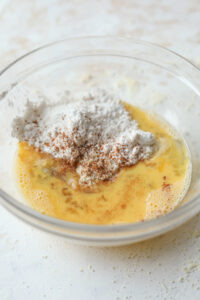 A glass bowl filled with wet & dry ingredients to make a cake.