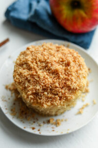 A piece of cake on a white plate. There is a crumble on top of the cake.