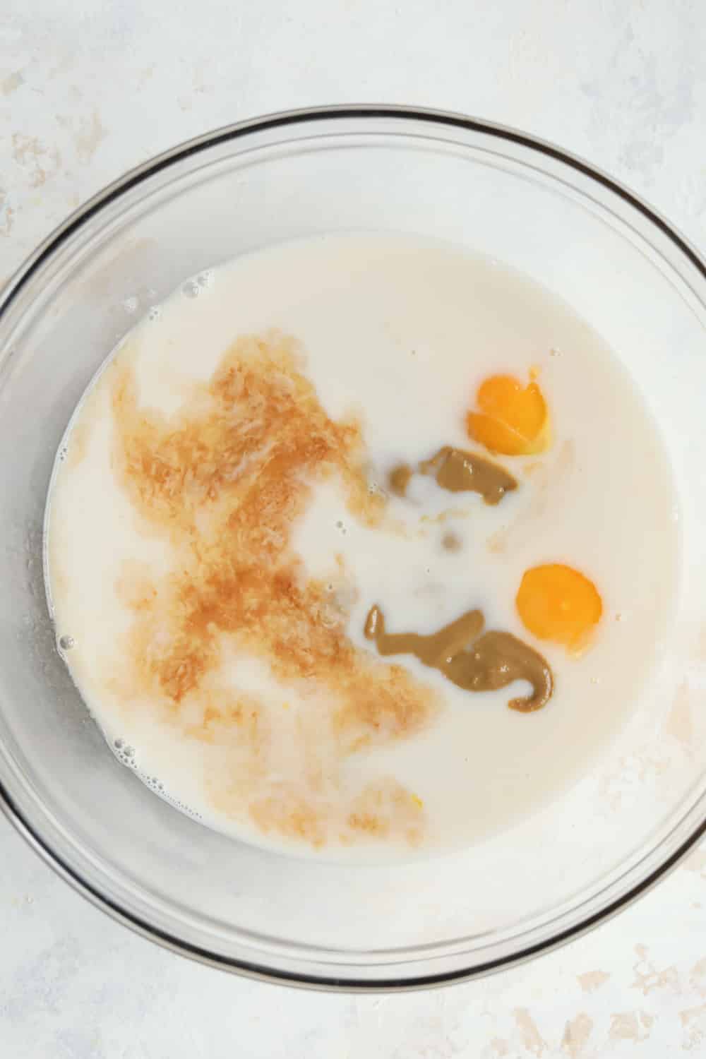 A glass bowl filled with nut butter, eggs, milk, and vanilla extract.