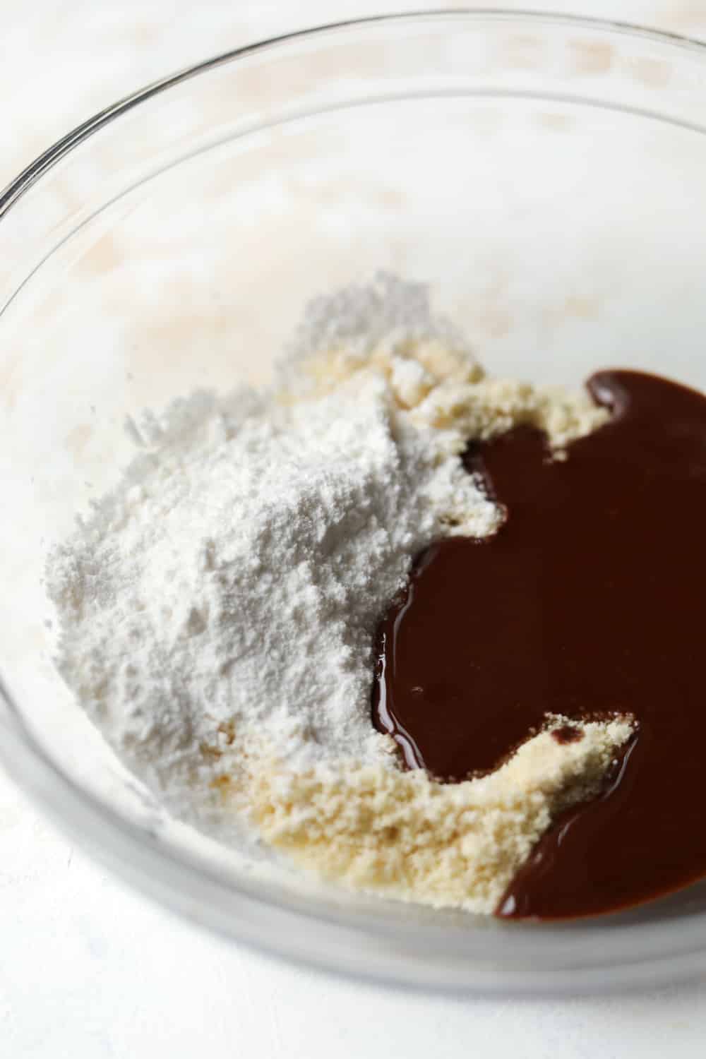 A glass bowl with almond flour, sugar substitute, and a sugar-free chocolate syrup inside of it.