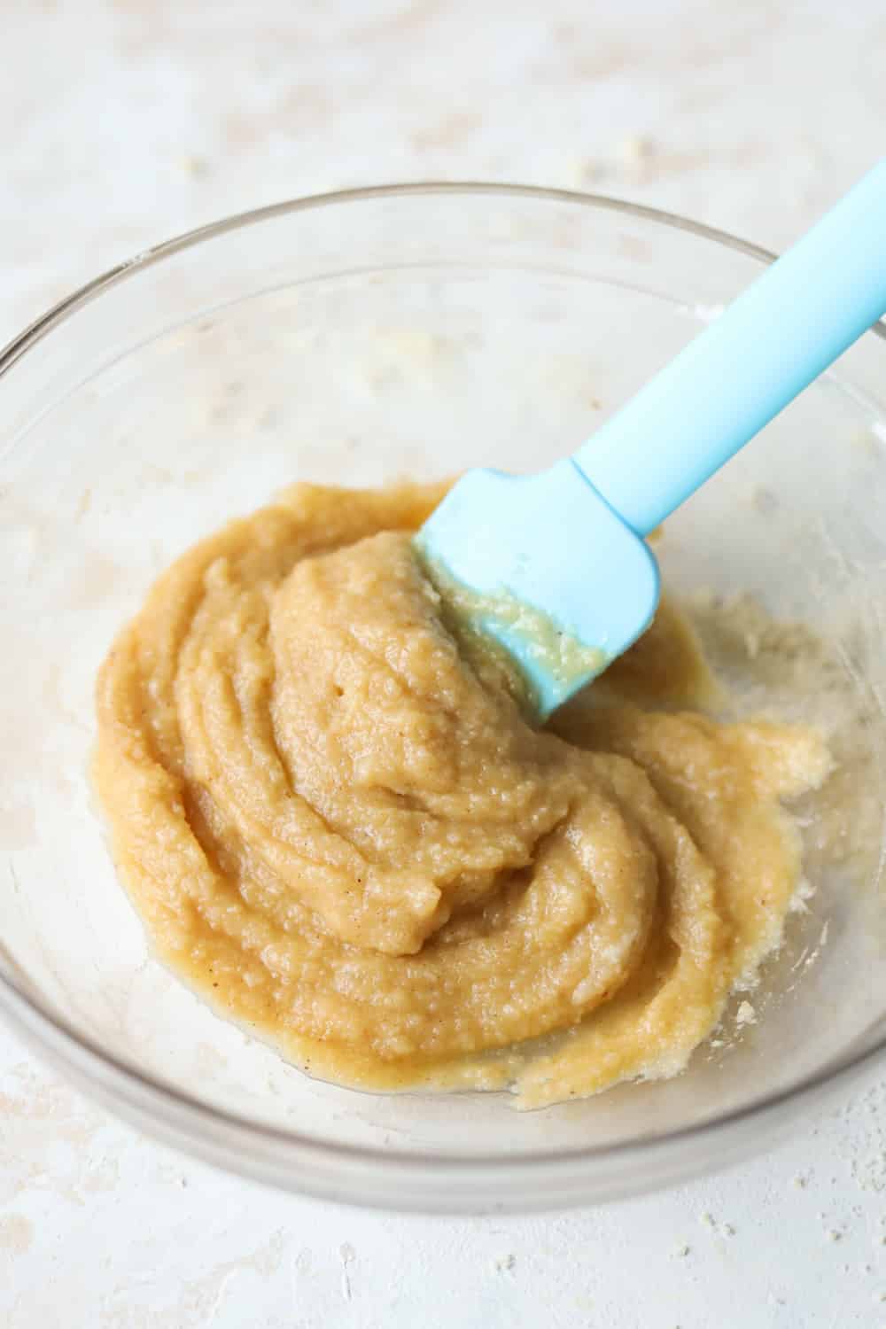 Cake batter in a glass bowl with a blue spatula set in the batter.