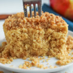 An apple crumble spiced cake cut in half with a fork inserted into the cake.