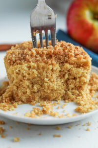 An apple crumble spiced cake cut in half with a fork inserted into the cake.