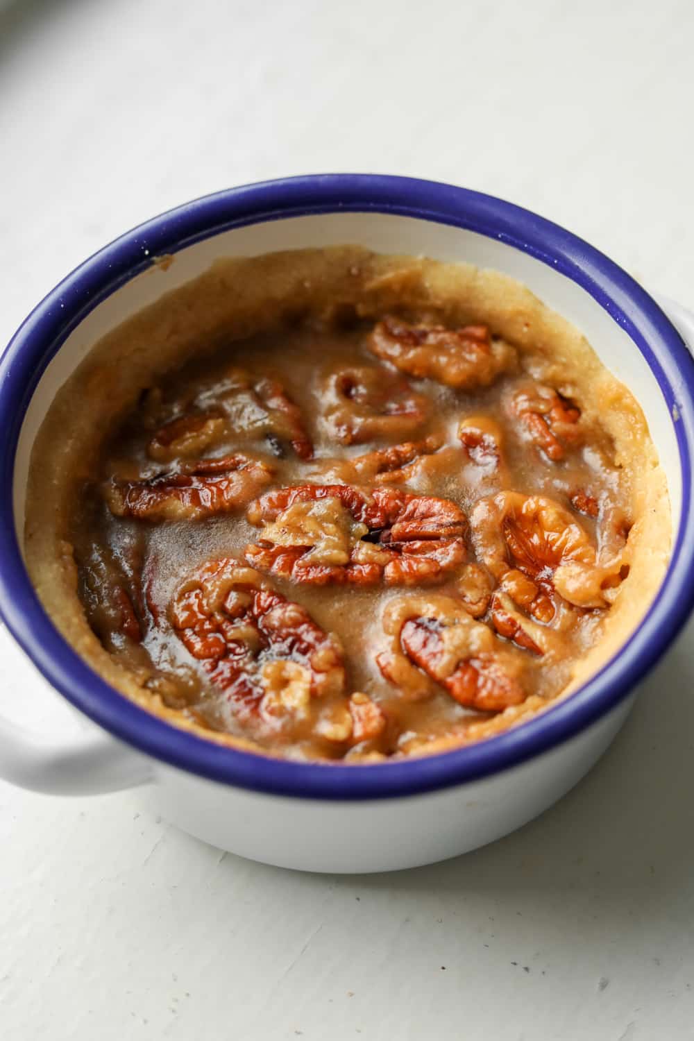 A pecan pie in a white bowl with a blue rim. The filling of the pie is still wet.