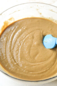 A thick batter inside of a glass bowl. There's a blue spatula inside of the bowl.