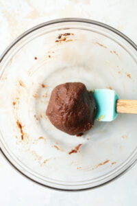 A glass bowl filled with brownie dough. There is a turquoise spatula inside of the bowl.