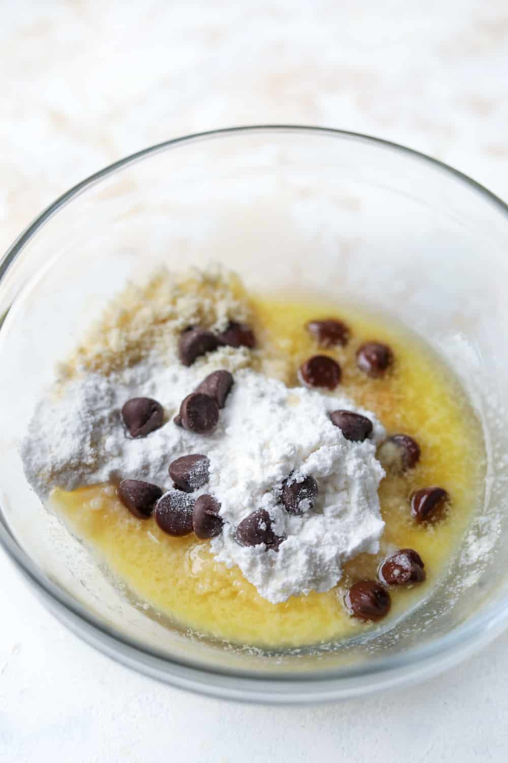 A glass bowl with almond flour, sugar substitute, butter, and sugar free chocolate chips inside of it.