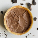 Chocolate pie on a white table with pieces of chocolate around it.