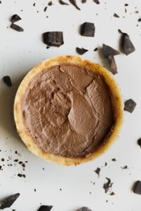 Chocolate pie on a white table with pieces of chocolate around it.