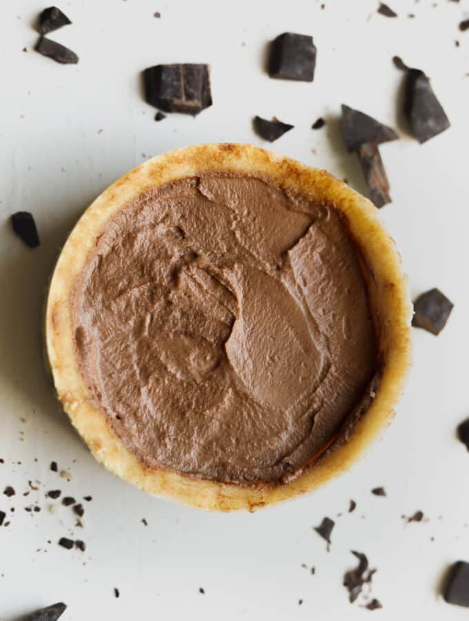 Chocolate pie on a white table with pieces of chocolate around it.