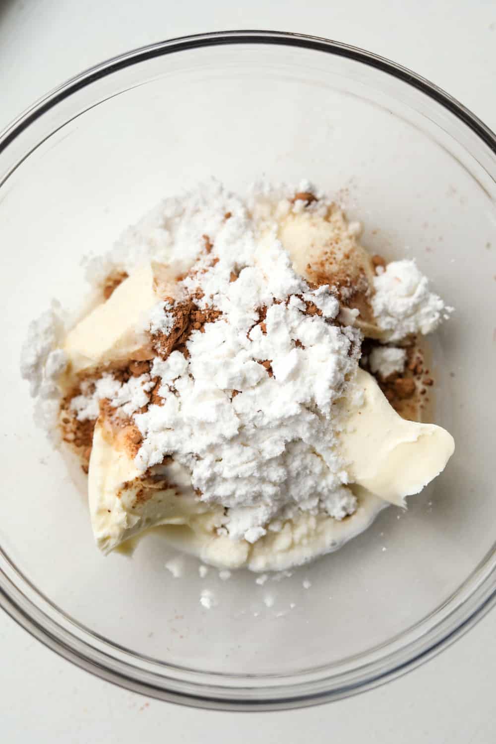 Mascarpone cheese, cocoa powder, sweetener, and almond milk in a glass bowl.