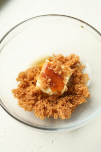 Butter on top of brown sugar in a glass bowl.